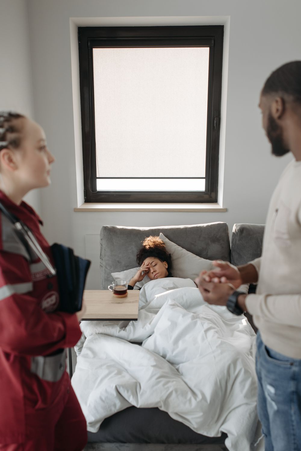 A paramedic checks on a woman lying on a hotel-room sofa, with her companion nearby